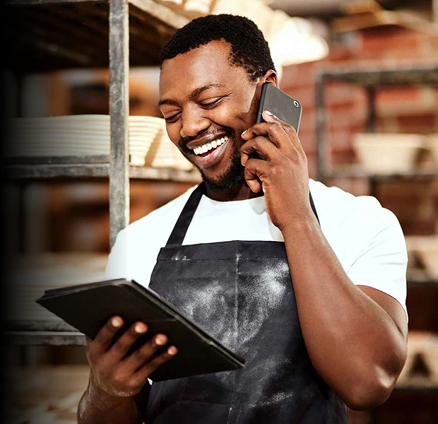 A man in a smock on the phone while using a tablet